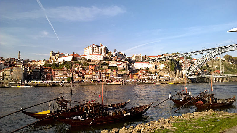 View of Porto showing boats on a river and a tall bridge leading into the city.