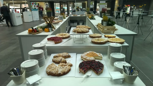 Several tables in the lunch area with multiple cakes on display.